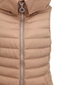 Chaleco acolchado beige con cuello alto, costuras horizontales y una cremallera plateada. Textura suave y acolchada; sin mangas; detalles de diseño minimalistas.