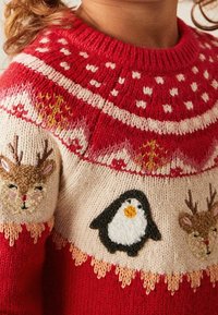 Maglione rosso lavorato a maglia con pois bianchi, motivi intricati e disegni ricamati di renne e un pinguino sul petto.