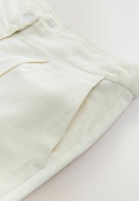 Bermuda di lino color crema chiaro con vita piatta e tasche laterali; texture liscia e dettagli di design minimalisti.