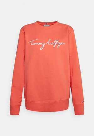 Sweat-shirt corail à manches longues avec col rond, logo script "Tommy Hilfiger" blanc centré sur le devant et petit logo drapeau près du poignet gauche.