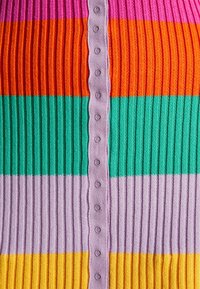 Top de punto a rayas multicolor con relieve, que presenta rayas horizontales en rosa, naranja, verde, morado y amarillo, con una fila de botones en el centro.