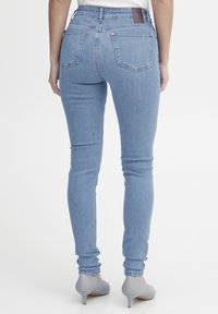 Világoskék farmernadrág magas derekú kivitelben, slim fit fazonnal és öt zsebbel. Jellemzője egy barna bőr folt a deréknál és formázott varratok.