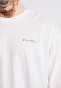 Witte t-shirt met korte mouwen, gemaakt van zachte katoen, met een lichtblauwe Columbia-logo op de linkerkant van de borst. Glad textuur, ontspannen pasvorm.