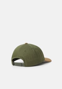 Grøn stofkasket med en beige skygge, justerbar rem bagpå og en afrundet krone med ventilationshuller.