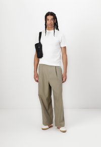 White short-sleeve T-shirt, loose olive green trousers, black crossbody bag, and white shoes with red stripes. Minimalist design, casual look.