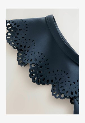 Tumesinine topp, millel on laineline, laserlõikega pitsikaelus. Sile tekstuur, ilma varrukateta disain, serval on peened tilgakujulised mustrid.