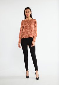 Rode en gele geblokte langemouwen top gecombineerd met zwarte leggings en hoge hakken. De top heeft een ontspannen pasvorm en een ronde halslijn.