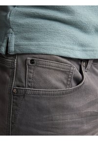 Jeans grises con una cinturilla texturizada y un bolsillo lateral, con herrajes negros para el cierre. Combinando con una camisa texturizada de color azul claro.