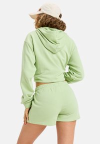 Cazadora corta de color verde claro con diseño de capucha trasera, combinada con pantalones cortos a juego. Textura suave y detalle de cinturilla elástica. Tejido de mezcla de algodón.