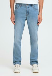 Jeans de denim azul claro con un diseño de corte recto, cinco bolsillos y un sutil desgaste. Llevados con zapatillas blancas.