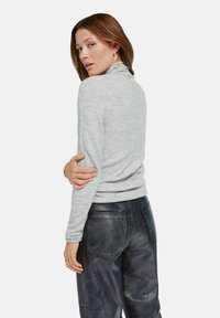 Szary sweter z golfem wykonany z dzianiny o dopasowanym kroju, w połączeniu z ciemnymi skórzanymi spodniami z tylnymi kieszeniami i gładką fakturą.