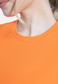 T-shirt ajusté orange avec un col rond et une texture lisse. Détail de couture visible le long du col.