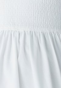 Balta suknelės medžiaga su tekstūruotu, raukšlėtu liemeniu ir sugriebtą sijoną, pagaminta iš lengvos medžiagos su lygiu paviršiumi.