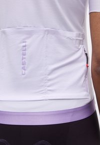 Κοντινό πλάνο ενός ατόμου που φοράει λευκό ποδηλατικό jersey με μωβ τελείωμα, πίσω τσέπες και το λογότυπο "CASTELLI" στην αριστερή τσέπη.