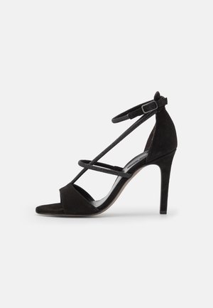 Schwarze Wildledersandaletten mit hohen Absätzen, gekreuzten Knöchelriemen und offenem Zehendesign. Glatte Textur und schlanker Stilettoabsatz.