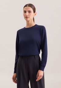Maglione azzurro scuro a maniche lunghe realizzato in tessuto morbido con scollatura a girocollo, abbinato a pantaloni scuri a vita alta. Design minimalista.