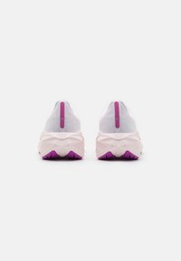 Weiße Sportschuhe mit einer strukturierten Oberfläche, pinken Akzenten und einer klobigen Sohle mit einem lila Profilmuster. Die Rückansicht zeigt eine schlanke Fersenschlaufe.