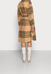 Tkaninowy płaszcz w kratę w odcieniach brązu, pomarańczy i zieleni; z paskiem w talii, mankietami na guziki, o średniej długości, zestawiony z beżowymi botkami do kolan.
