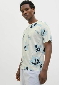 Camiseta de algodón con una base gris claro y grandes patrones florales en azul y negro, cuello redondo y mangas cortas. Textura suave.