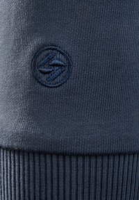 Maglione lavorato a maglia blu navy con orlo a coste testurizzato e logo circolare ricamato che presenta un design stilizzato nello stesso colore del filo.