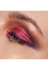 Stängd öga med glittrande rosa och lila metalliskt ögonskugga, naturlig ögonbryn och långa, böjda ögonfransar på ljus hud.