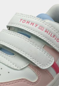 Baskets blanches avec accents roses, sangles à scratch et col rembourré bleu. Présentent un logo sur la sangle et des détails perforés.