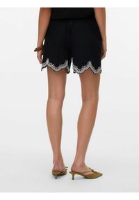 Zwarte shorts met een gekartelde zoom, versierd met witte bloemenborduursels. Lichtgewicht stof met een elastische tailleband.