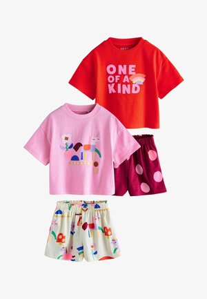 To sæt børnetøj: rød T-shirt med "ONE OF A KIND" og regnbue, pink T-shirt med enhjørning, kombineret med shorts med prikker og enhjørning-tryk.