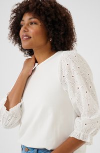 White top with textured lace puff sleeves featuring circular patterns and small cutouts. Simple round neckline and relaxed fit.