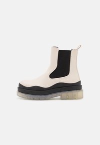 Cream leather ankle boot with black elastic side panel, thick black sole, and translucent outsole. Features a pull tab at the back.