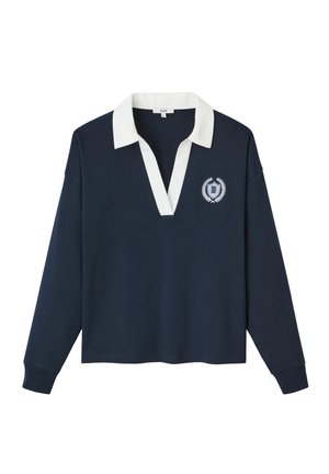 Pull navy avec un col contrastant blanc, à manches longues et en V. Présente un emblème brodé sur le côté gauche.