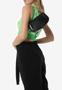 Borsa in pelle nera con un design curvo e una tracolla in catena dorata, abbinata a una maglietta verde con fantasia e pantaloni neri.