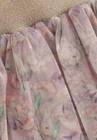 Blumen-Mesh-Stoff in zartem Pink mit grünen Akzenten verfügt über weiche Rüschen. Ein strukturiertes Goldgewebe ist oben sichtbar und schafft einen Kontrast.