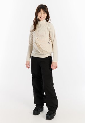 Beige fleece top met een half-zip kraag, gecombineerd met zwarte baggy broek en een gestructureerde crèmekleurige schoudertas. Zwarte voetbedekking maakt de outfit compleet.