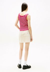 Rot-weiß gestreiftes Tanktop, figurnahes Design; kombiniert mit einem beigen Rock, der aufgesetzte Taschen zeigt. Schwarze Schuhe mit weißen Socken runden den Look ab.
