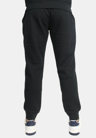 Pantaloni della tuta neri realizzati in un tessuto morbido, con vita elastica e gambe affusolate, abbinati a sneaker bianche e blu navy.