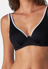 Reggiseno nero con una superficie liscia, caratterizzato da rifiniture bianche lungo il décolleté a scollatura profonda e spalline regolabili per una vestibilità confortevole.