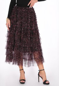 Fustă transparentă în straturi, de culoare bordeaux și cu imprimeu animal. Prezintă mai multe volane și un brâu ajustat, asortată cu sandale negre cu toc înalt.