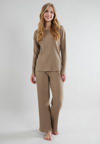 Beige, geribbelde lounge-outfit met een lange mouwen top en wijde broekspijpen. Zacht materiaal met een ontspannen pasvorm en zonder zichtbare hardware.