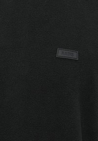 Svart fleece-genser med teksturert overflate, rund hals og et rektangulært sorte gummimerke med ordet "RAINS."