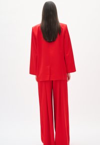 Roter maßgeschneiderter Blazer und weite Hose, glattes Material, lockere Passform, Mittelnähte am Blazer, klare Linien mit minimalistischer Gestaltung.