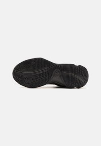 Semelle d'une chaussure de sport noire avec des motifs de grip texturés et un logo swoosh visible, présentée sur un fond neutre.