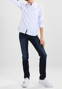 Jasnoniebieska, w poziome paski, koszula z długim rękawem, z detalem kieszeni. Para ciemnoniebieskich dżinsów i białe trampki dopełniające strój.