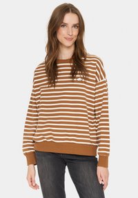Sweatshirt cu dungi maro și alb, cu o croială lejeră, manșete ribatate și o mică insignă în formă de nor pe piept. Textură de țesătură moale.