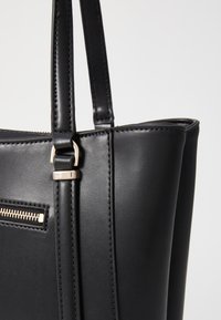 Borsa a tracolla nera in pelle con due manici robusti, dotata di tasca con zip e dettagli in metallo argentato. Texture liscia e linee pulite.