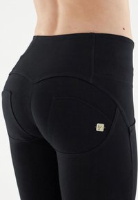 Leggings negros de tiro alto con una textura suave, que presentan costuras curvadas y una pequeña etiqueta de logo en la zona del bolsillo trasero.