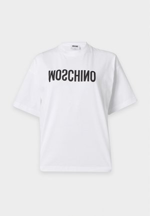 Femme portant des lunettes de soleil noires, un t-shirt blanc avec le texte MOSCHINO inversé, une jupe asymétrique rayée blanche et des sandales noires à talons hauts.