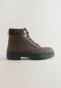 Braune Leder-Ankle-Boots mit einem Wildlederkragen, metallenen Ösen, einer abgerundeten Zehenpartie und einer robusten schwarzen Gummisohle. Zudem verfügt er über eine Zuglasche an der Rückseite.