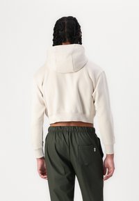 Cropped cream hoodie with a drawstring hood, ribbed cuffs, and a raw hem. Paired with deep green pants featuring a back pocket.
