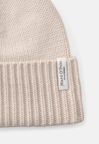 Strikket lue i myk lys beige med ribbet tekstur. Har et lite hvitt merke med "Marc O'Polo"-logo.